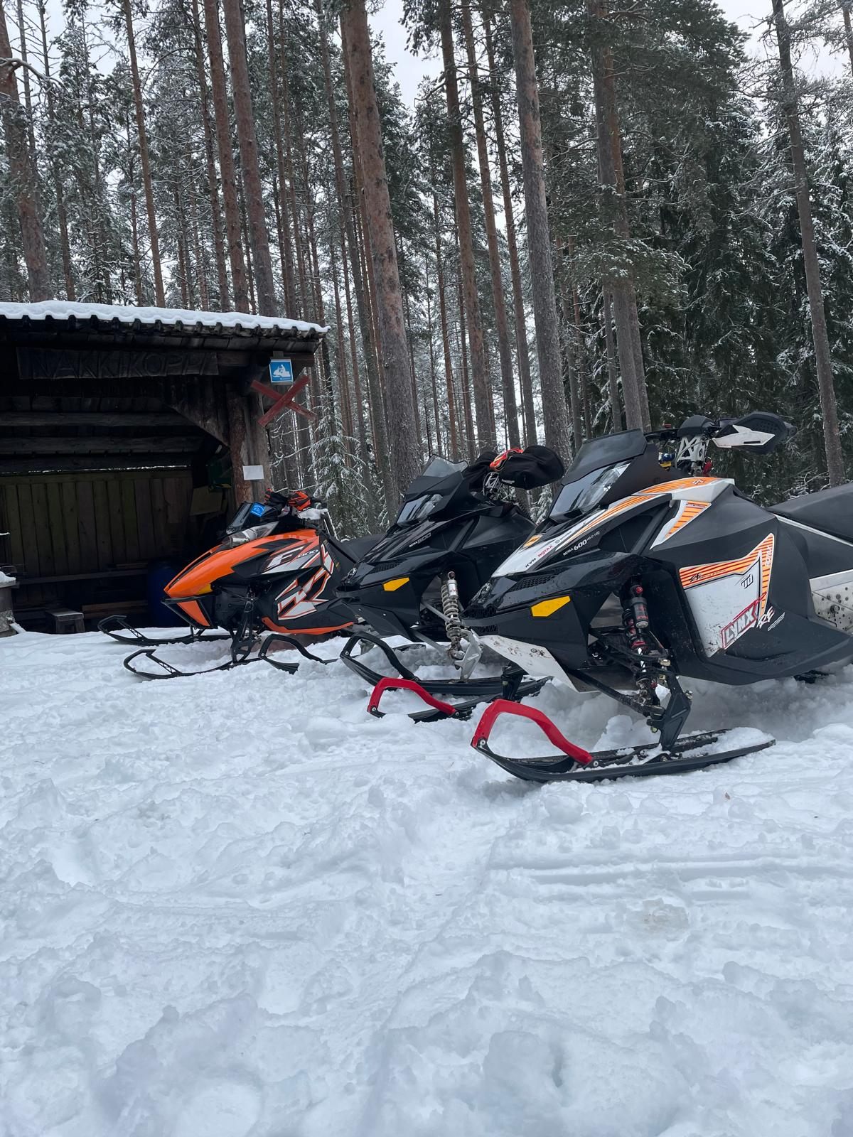 Kolme moottorikelkkaa lumessa, iskunvaimentimet näkyvissä